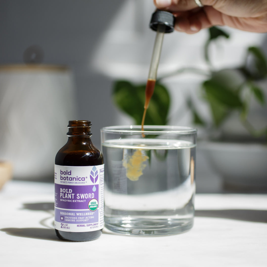 Bottle of Bold Plant Sword in front of a hand dropping drops of liquid extract into a glass