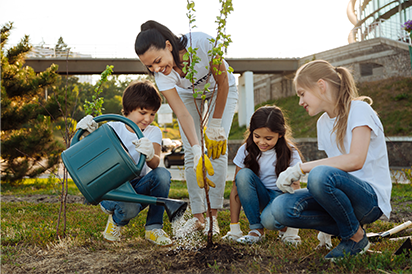 woman and three children watering a small tree